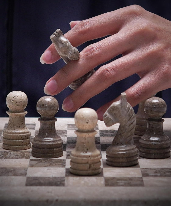 Hand holding a stone chess piece over a chessboard with other pieces.
