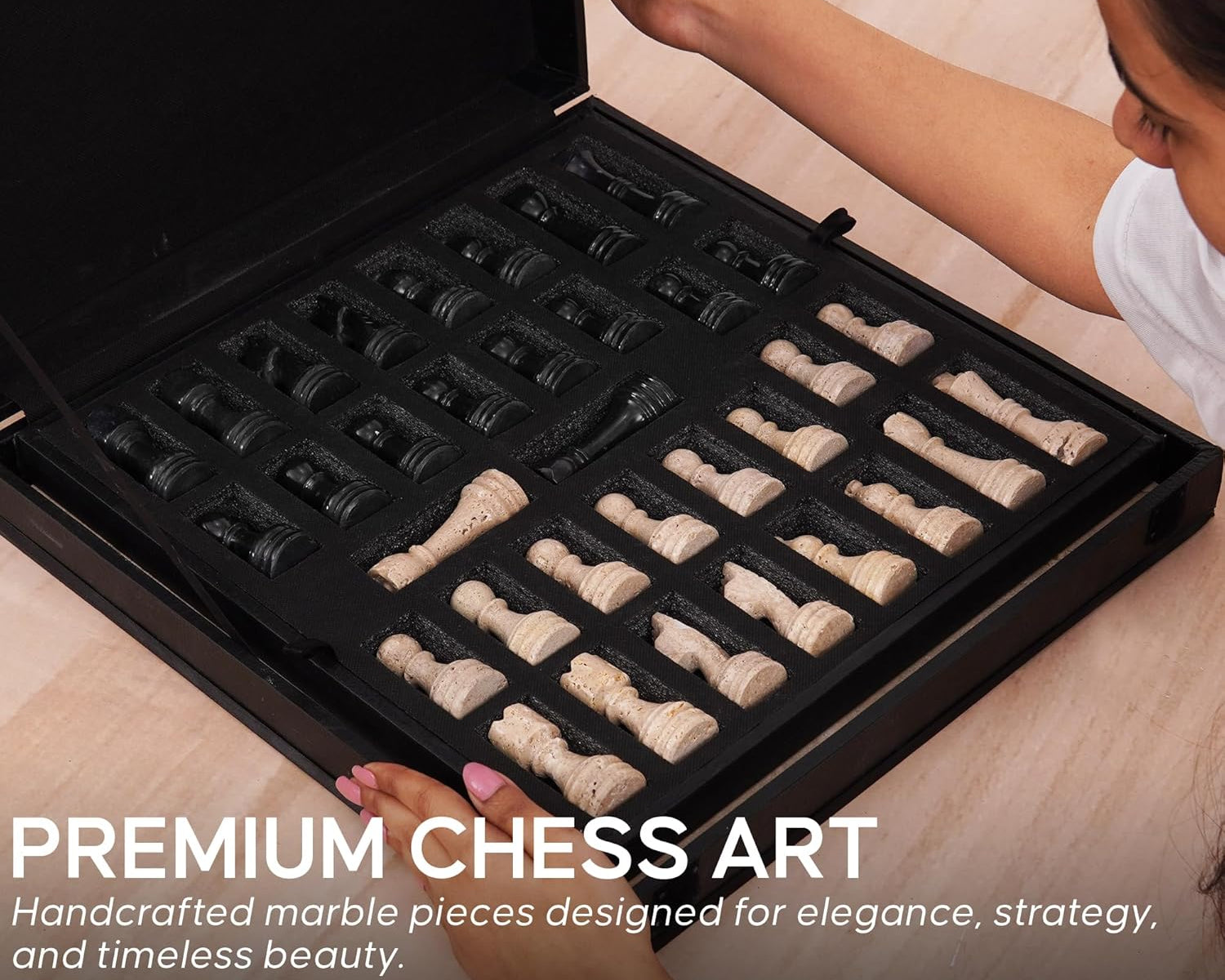 Person opening a black chess set box containing marble chess pieces.