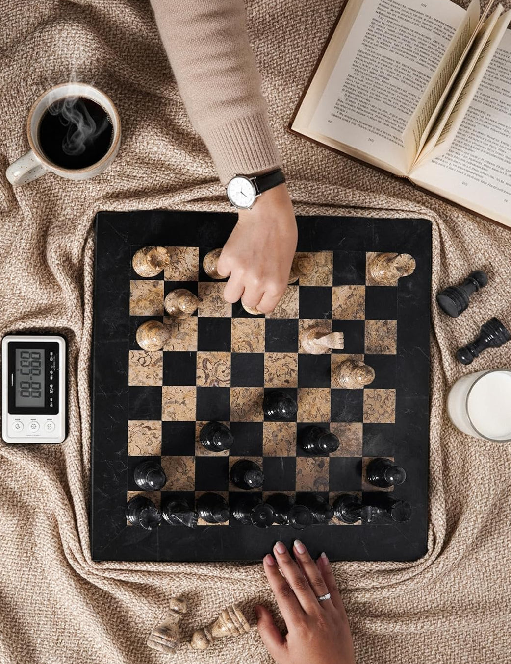 Person playing a game of checkers on a checkered board with a cup of coffee and book in the background.